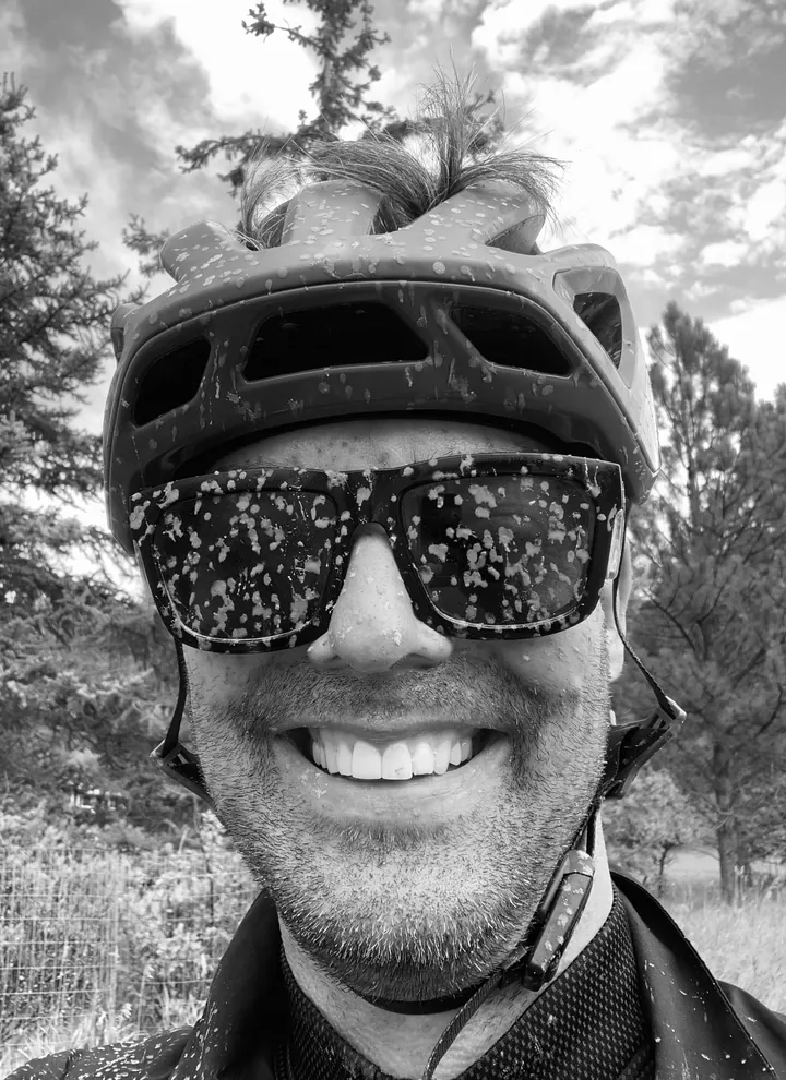 Kevin Miller grinning on a trail, with mud on his helmet and sunglasses