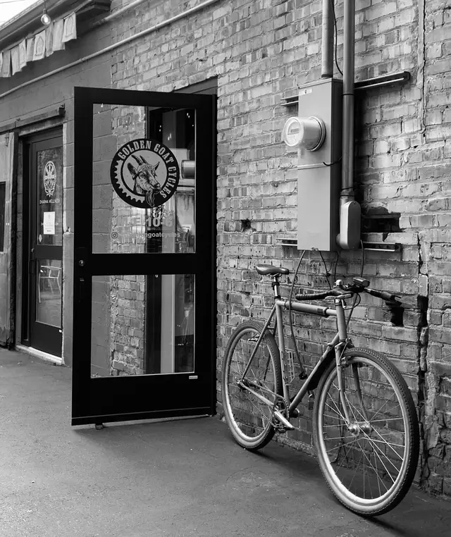 Golden Goat Cycles logo on the shop's glass door, with a bike leaning against the brick wall