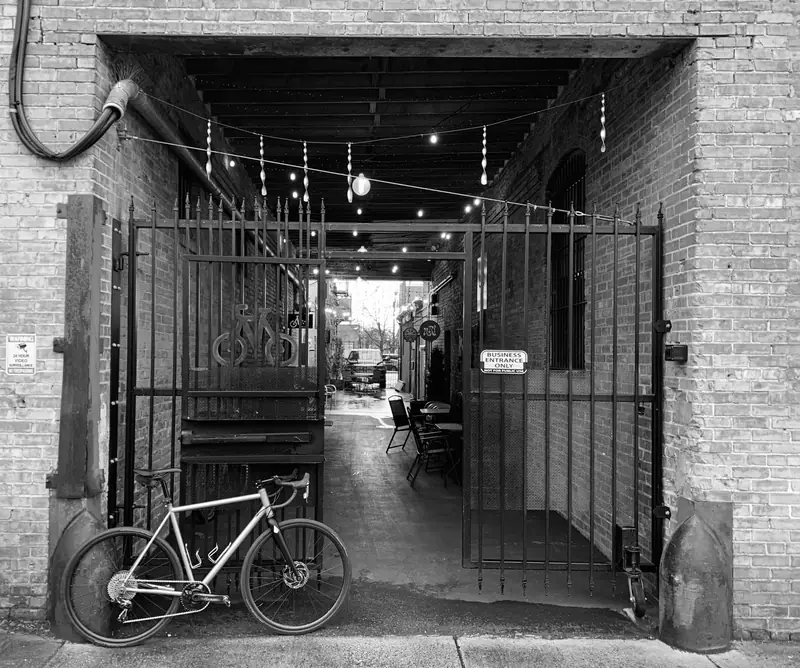 Iron gate leading into a brick passage with string lights and a bike leaning against the wall