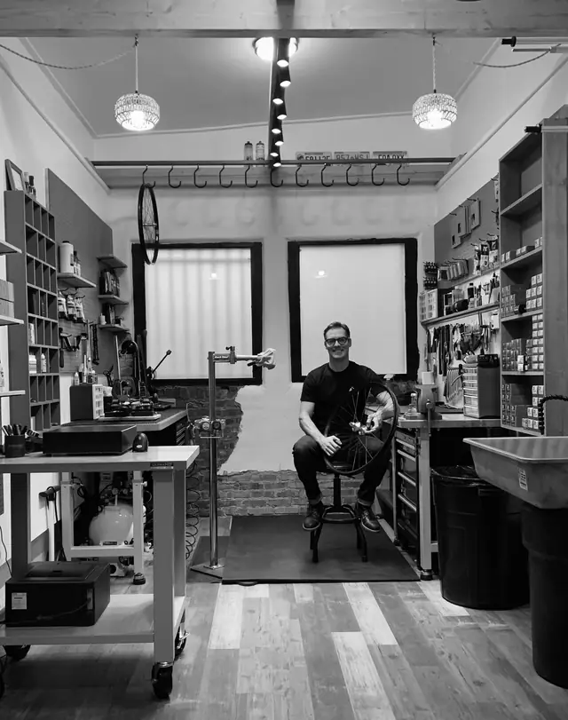 Kevin sitting between the parts shelves and repair stand at Golden Goat Cycles